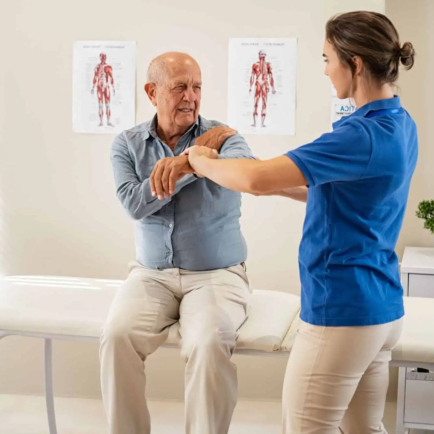 A physical therapist assists an older man seated on an exam table with arm stretches for pain management in a medical office decorated with anatomical charts.